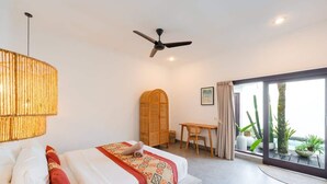 Une chambre à coucher comprenant un lit, un bureau, un ventilateur de plafond et une vue sur des plantes, visible à travers une porte coulissante.