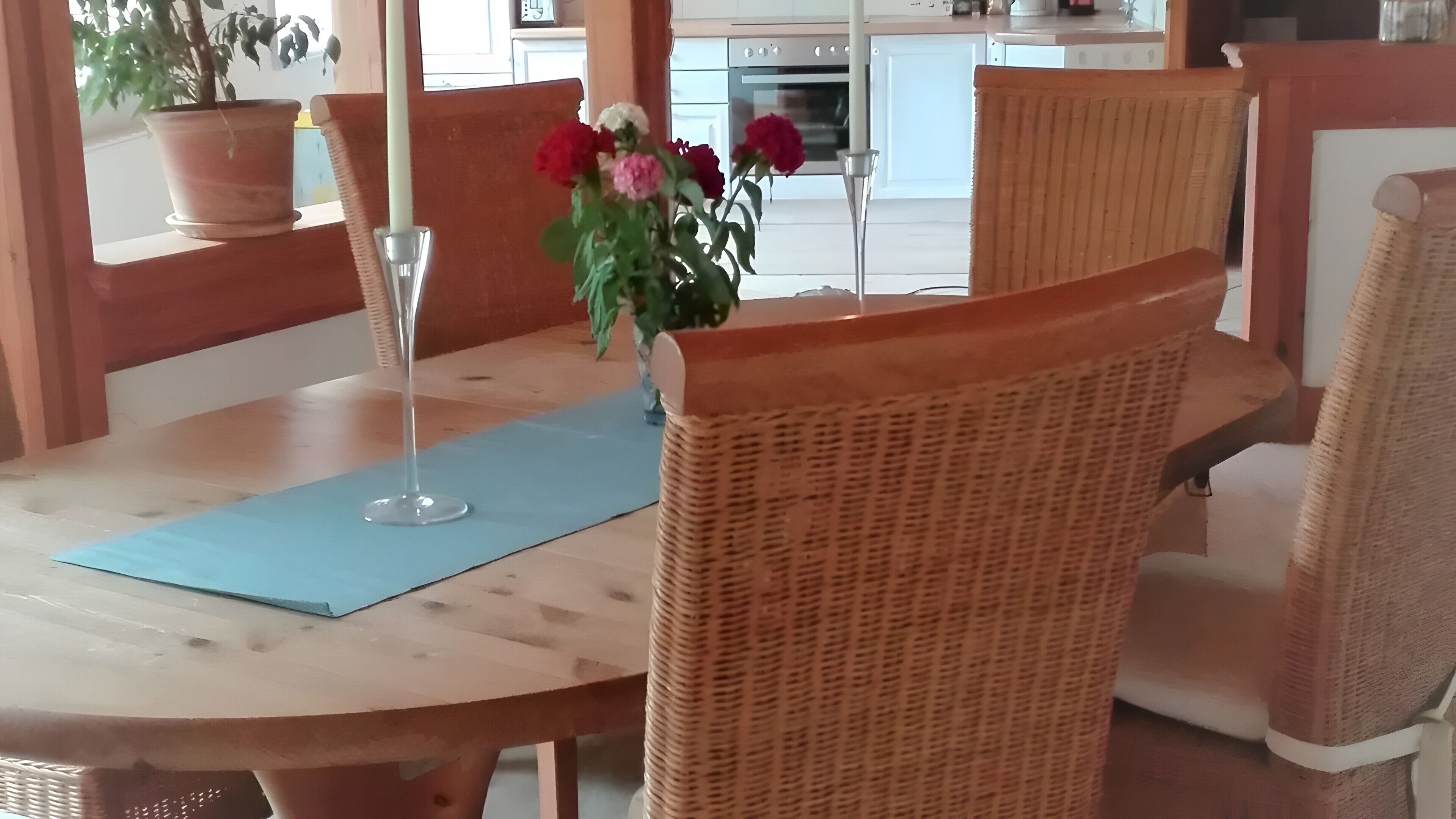A dining table with chairs, a vase with flowers, and a potted plant.