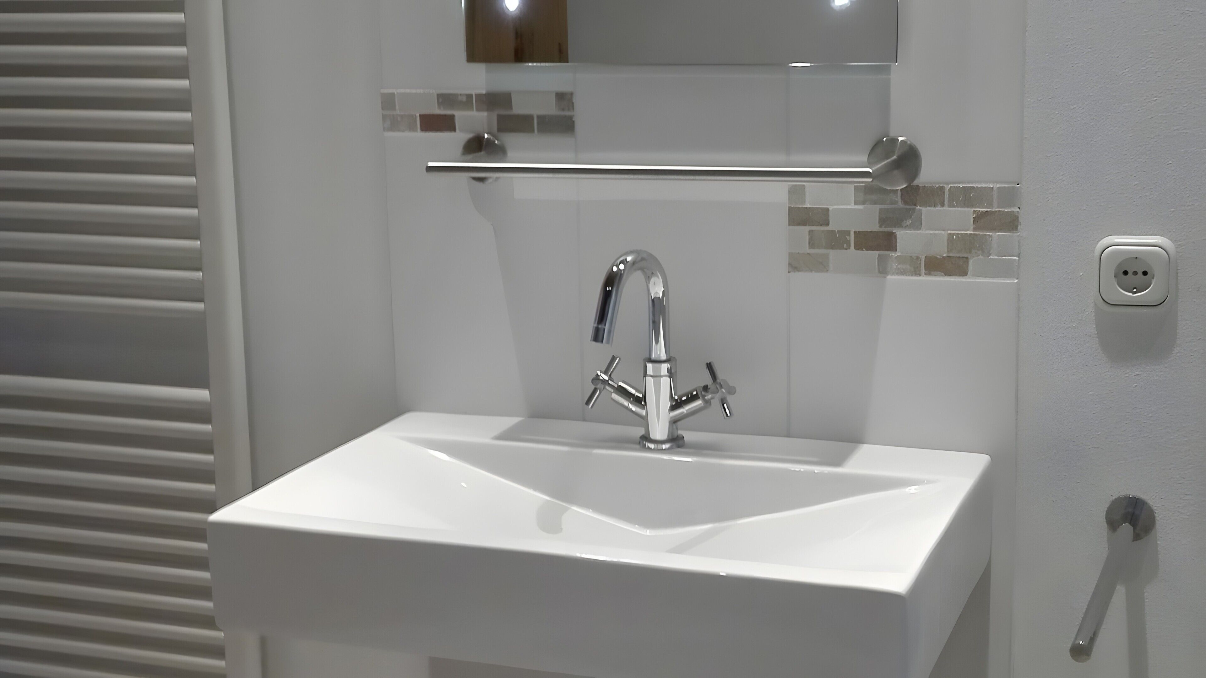 Ein Badezimmer mit einem weißen Waschbecken, einem Chromarmaturen und einem Spiegel darüber.