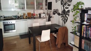 Ett modernt kök med vita skåp, ett matbord med stolar, en bokhylla och en stor väggmålning.