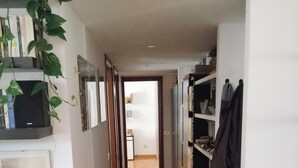 En smal hall med trägolv, en bokhylla på höger sida och en växt på vänster sida.