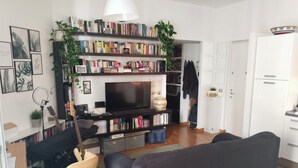 Ett vardagsrum med en tv, bokhyllor, en soffa, en gitarr och en växt.