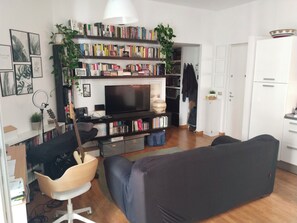 Een woonkamer met een televisie, boekenkasten, een bank, een gitaar en een plant.