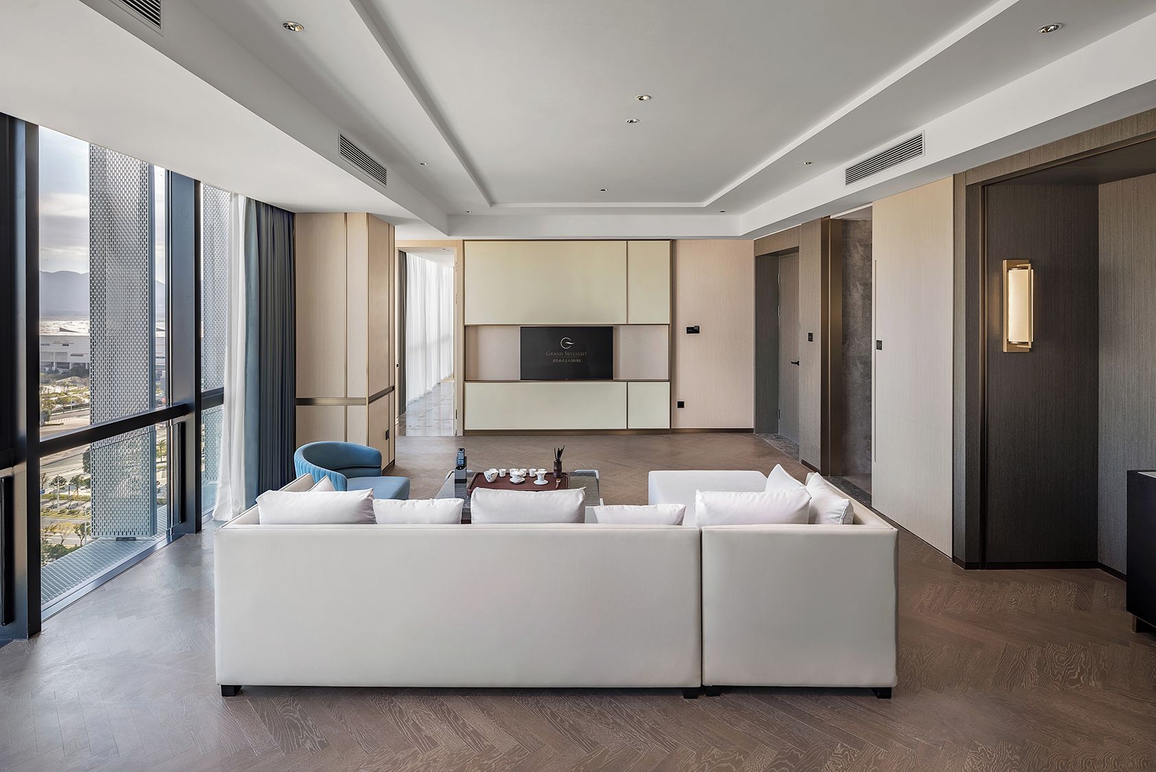 A modern living room with a large white sectional sofa, a blue chair, and a flat-screen TV mounted on a wall.