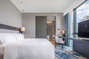 A hotel room with a large bed, a desk with a television, and a view of the city.