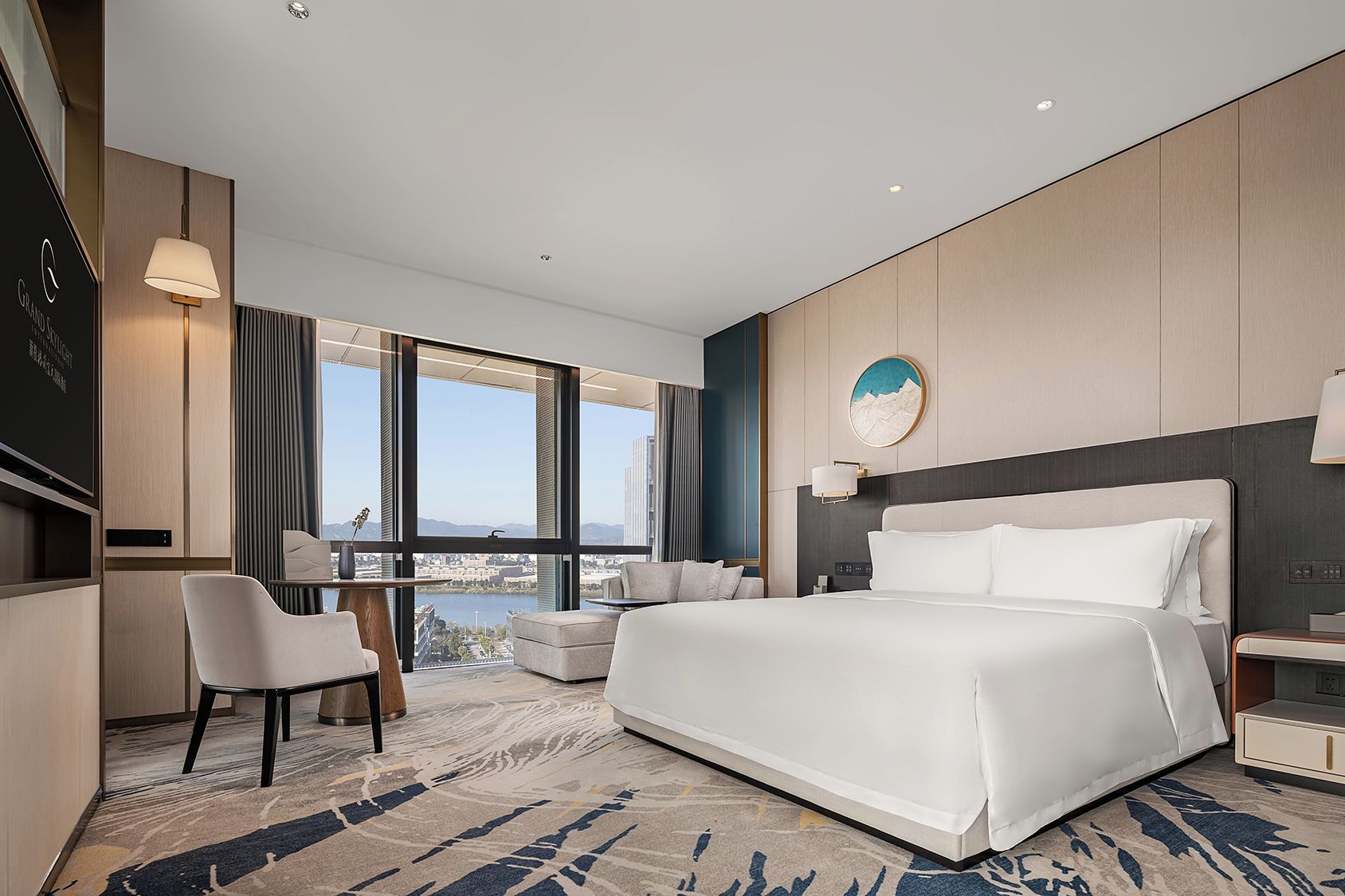 Quarto de hotel moderno com uma cama grande, uma escrivaninha, uma cadeira e vista para a cidade.