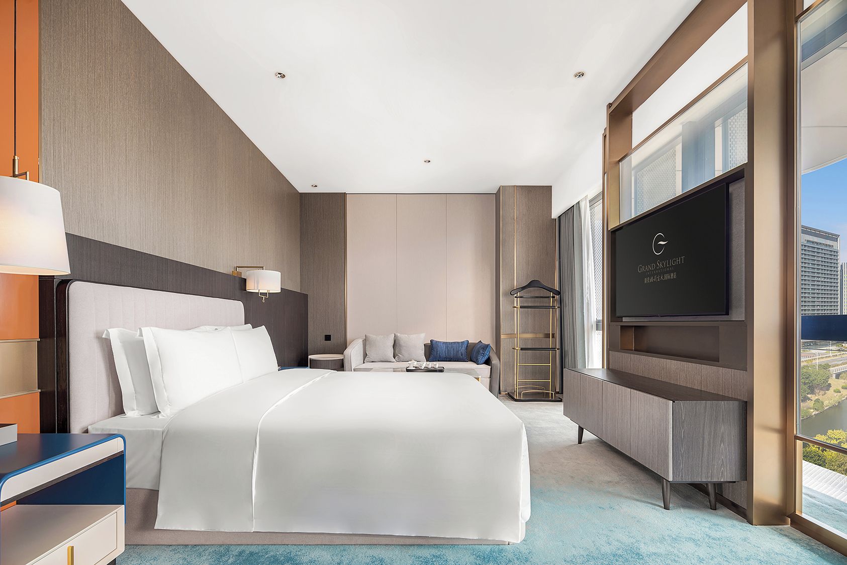 A modern hotel room with a large bed, a TV, and a view of a cityscape.