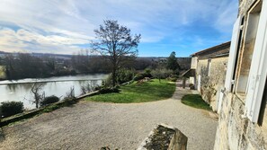 Ein Kiesweg führt zu einem Gebäude mit Blick auf einen Fluss und sanfte Hügel in der Ferne.