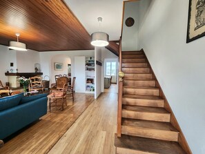 Ein geräumiger Wohnbereich mit einem blauen Sofa, Holzboden, einer Treppe und einem Bücherregal.