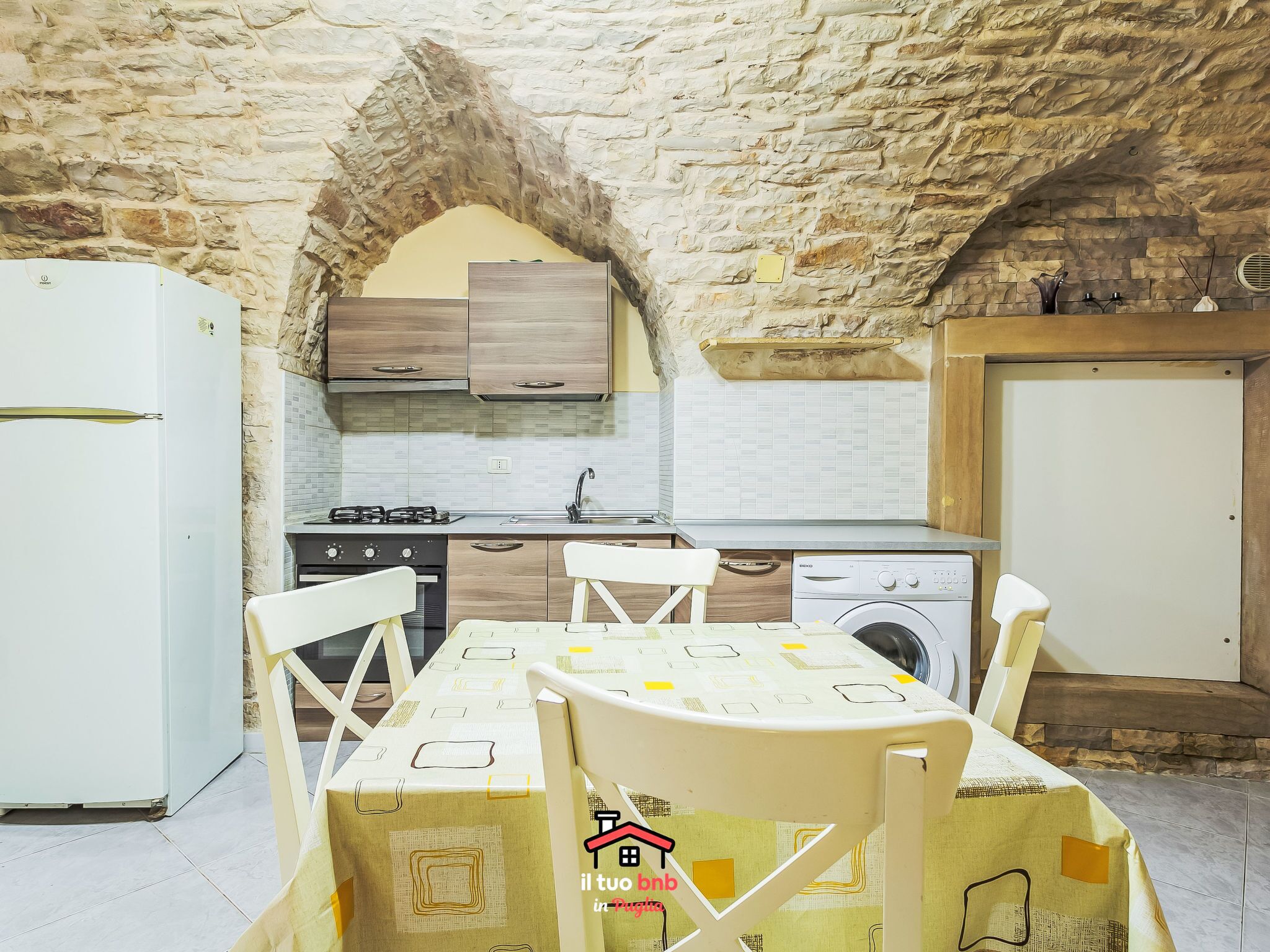 A compact kitchen with a stone wall, a washing machine, and a dining table with chairs.