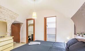 Une chambre à coucher avec un lit, une commode en bois, un miroir, un luminaire suspendu et une vue sur l’extérieur.