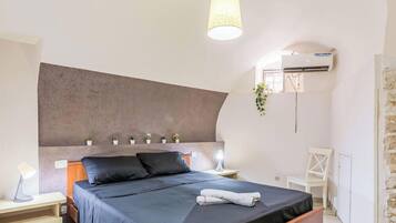 A bedroom with a bed, bedside lamps, a wall-mounted air conditioner, a small plant, and a white chair.