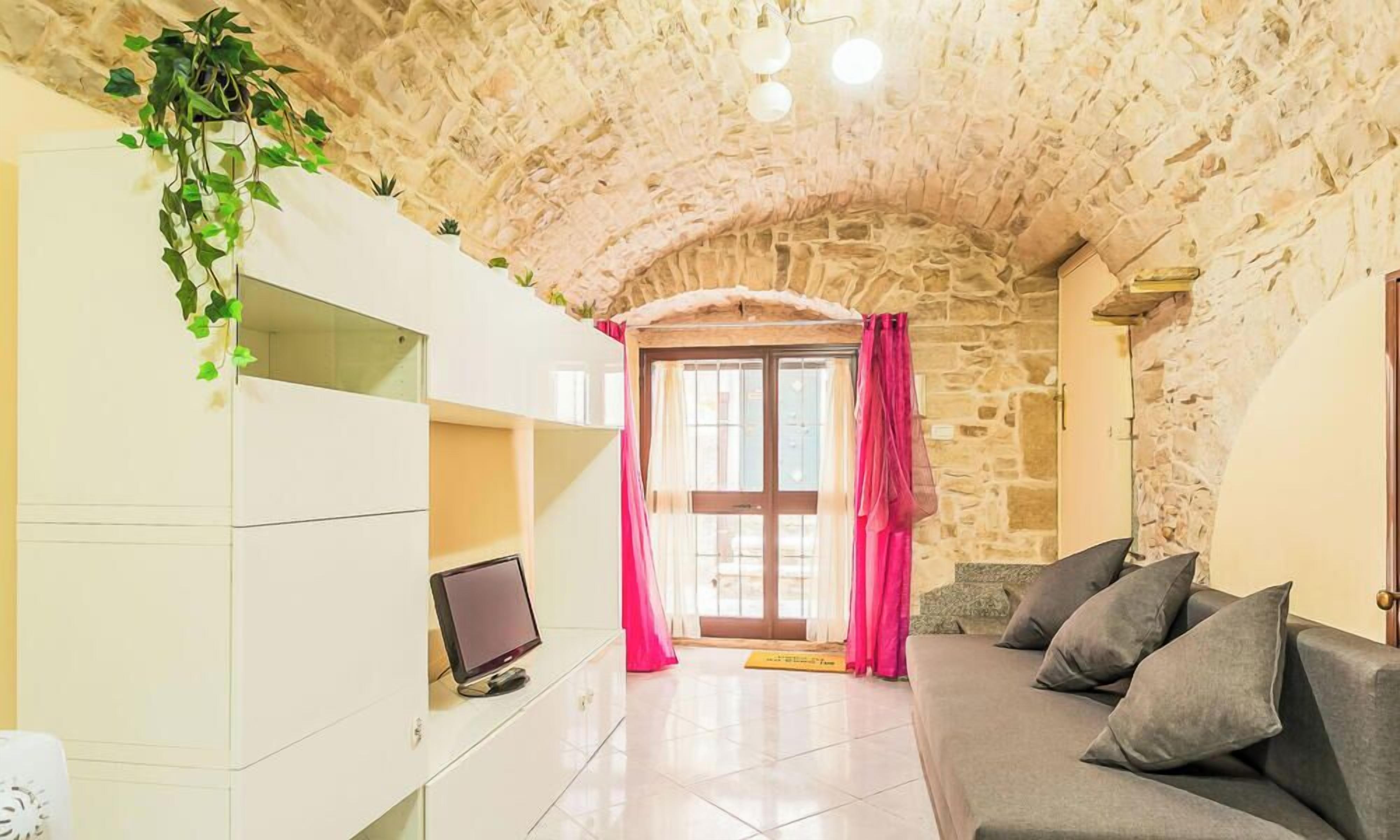 Ein Zimmer mit Steindecke, einer weißen Unterhaltungsanlage mit Fernseher, einem grauen Sofa und einer Tür mit rosa Vorhängen.