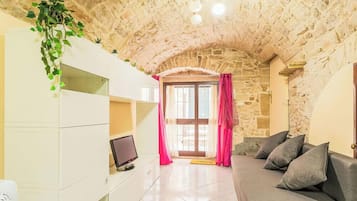 Ein Zimmer mit Steindecke, einer weißen Unterhaltungsanlage mit Fernseher, einem grauen Sofa und einer Tür mit rosa Vorhängen.
