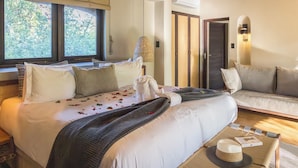 A hotel room with a bed, a sofa, a dining table, and a view of trees through the window.