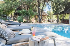 Zona de descanso junto a la piscina con tumbonas, un libro, una bebida y un sombrero.