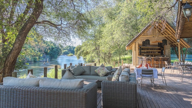 A wooden deck with wicker furniture, a bar area, and a view of a lake.