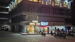 Ein Hotel mit einem gut sichtbaren Schild 'HOTEL APEX ROOMS', einem Geschäft im Erdgeschoss und geparkten Motorrädern davor.