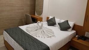 Ein Hotelzimmer mit Bett, Schreibtisch, Stuhl, Spiegel und Nachttisch mit Telefon.