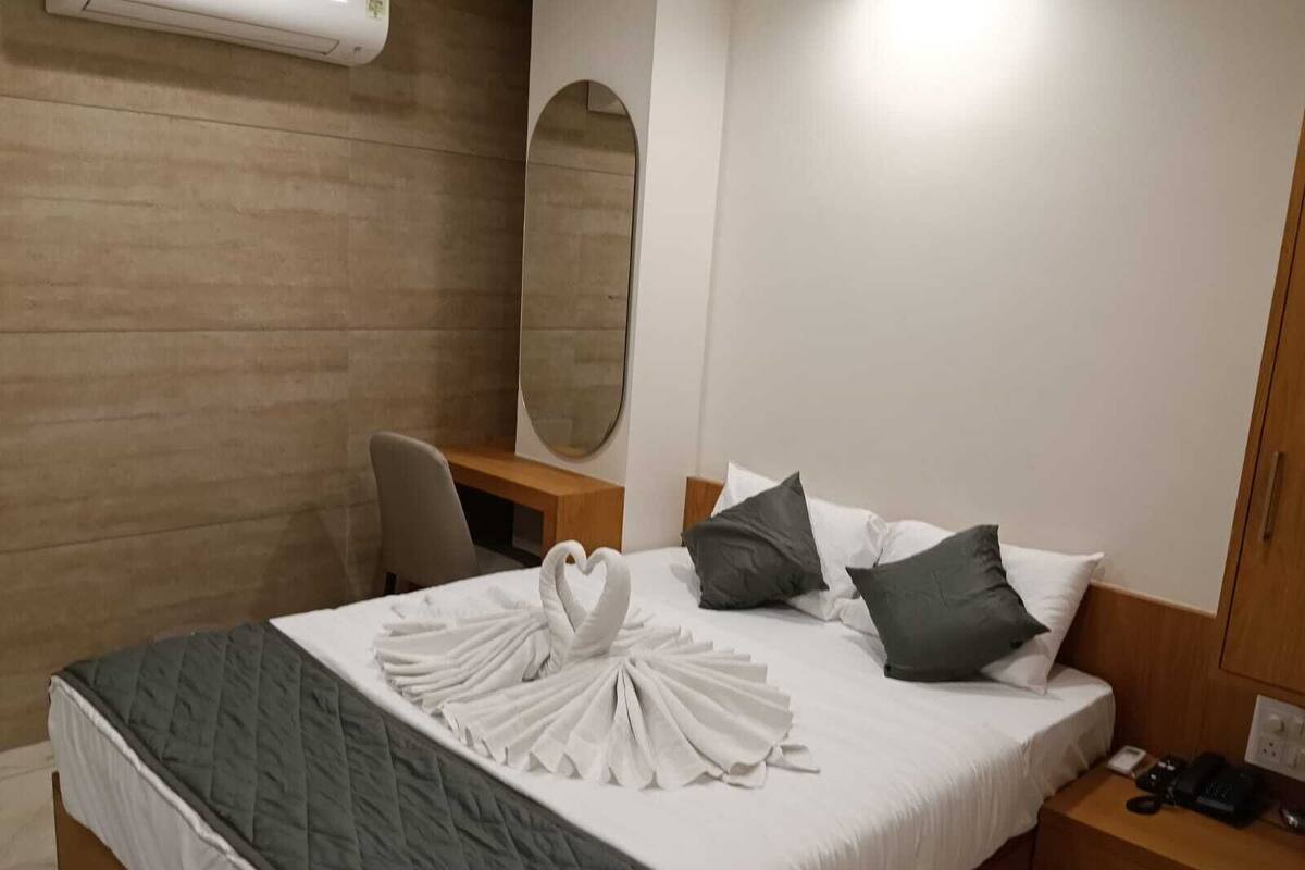 A hotel room with a bed, a desk, a chair, a mirror, and a bedside table with a phone.