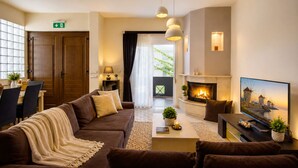Ein modernes Wohnzimmer mit Sofa, Couchtisch, Fernseher, Kamin und einem Essbereich mit Stühlen und Tisch.