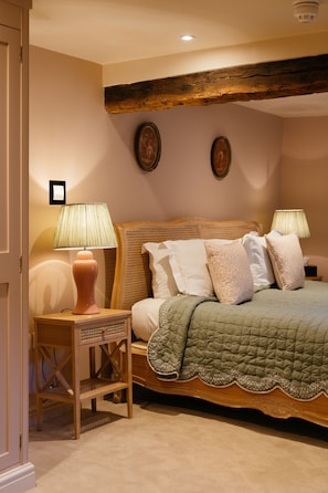 Un dormitorio con cabecera de madera, dos mesitas de noche con lámparas, una colcha verde acolchada y dos cuadros enmarcados en la pared.