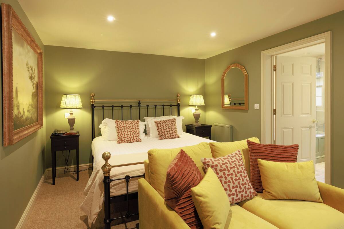 A bedroom with a bed, two bedside tables, a chair, a mirror, and a door.