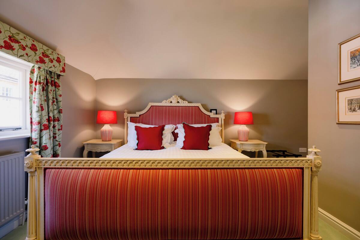 A bed with a red and white headboard, two bedside lamps, and a floral curtain.