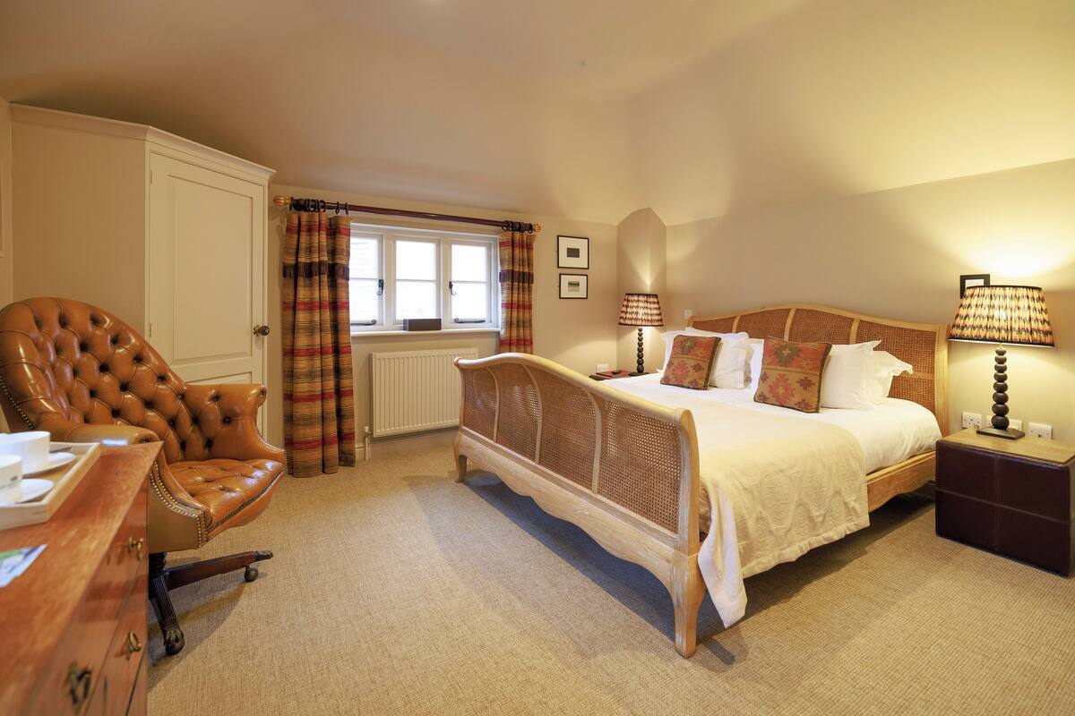 A bedroom with a bed, a chair, a dresser, a window with curtains, and a lamp.