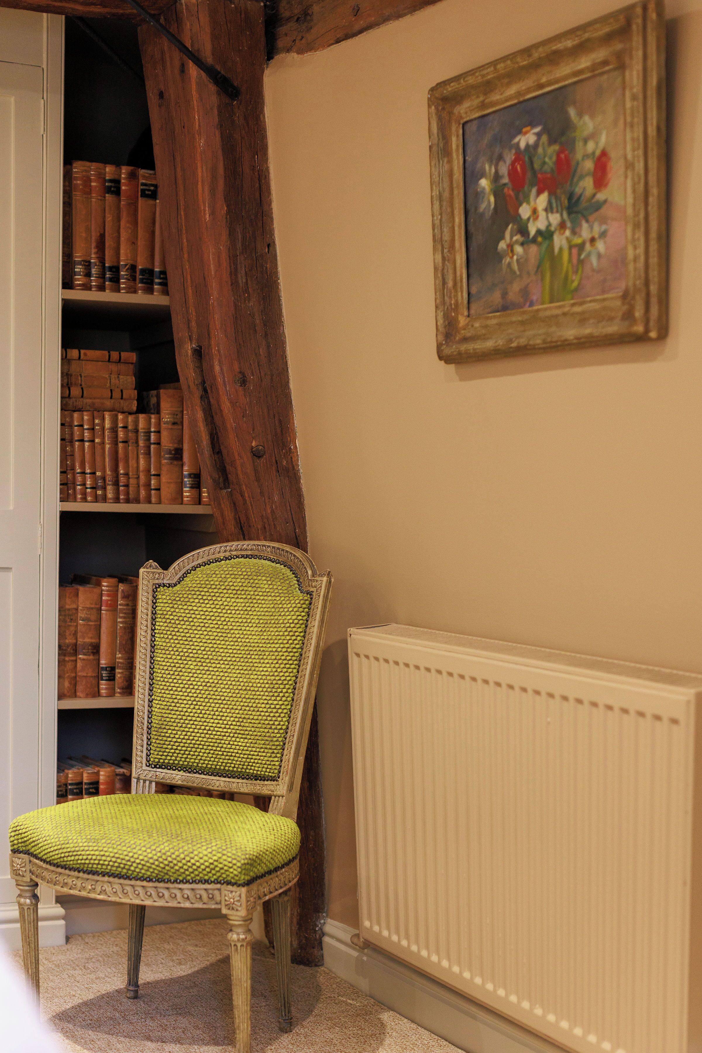 Une pièce avec une chaise en bois, une bibliothèque remplie de livres, un radiateur et un tableau accroché au mur.