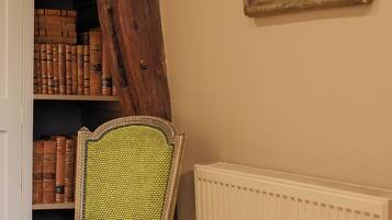A room with a wooden chair, a bookshelf with books, a radiator, and a painting on the wall.