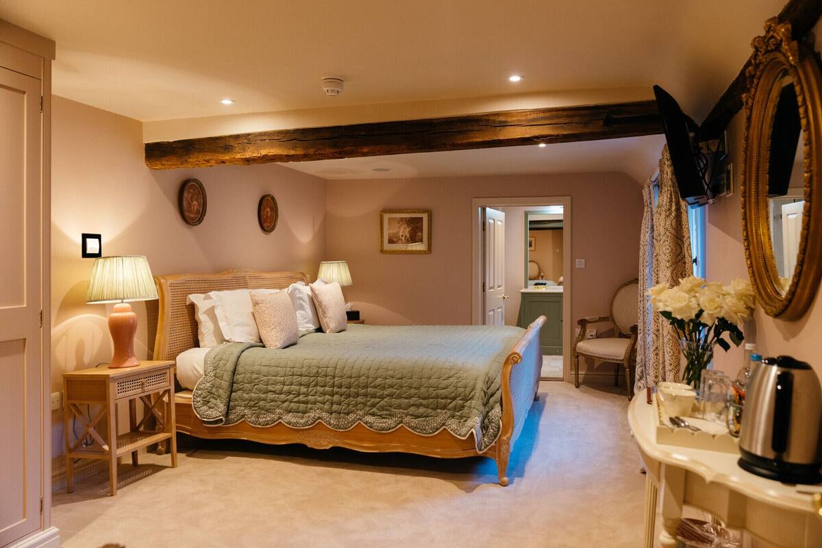A bedroom with a bed, bedside lamps, a dresser, a mirror, and a door leading to another room.