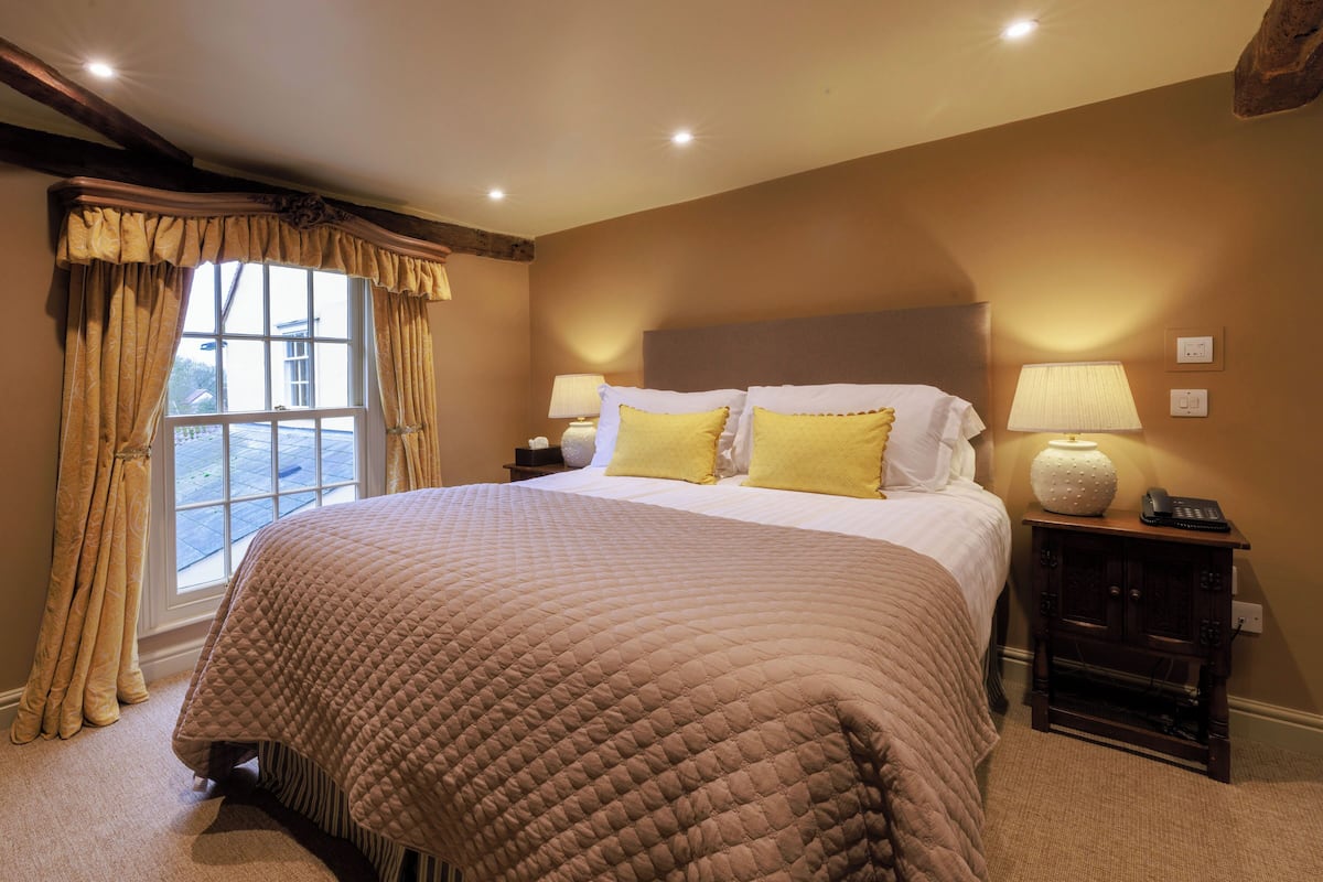 A bedroom with a large bed, two bedside lamps, a nightstand, and a window with curtains.