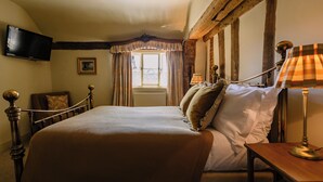 A bedroom with a bed, a television mounted on the wall, a window with curtains, and a lamp on a bedside table. - The Bildeston Crown (Bildeston)