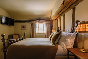 A bedroom with a bed, a television mounted on the wall, a window with curtains, and a lamp on a bedside table. - The Bildeston Crown (Bildeston)