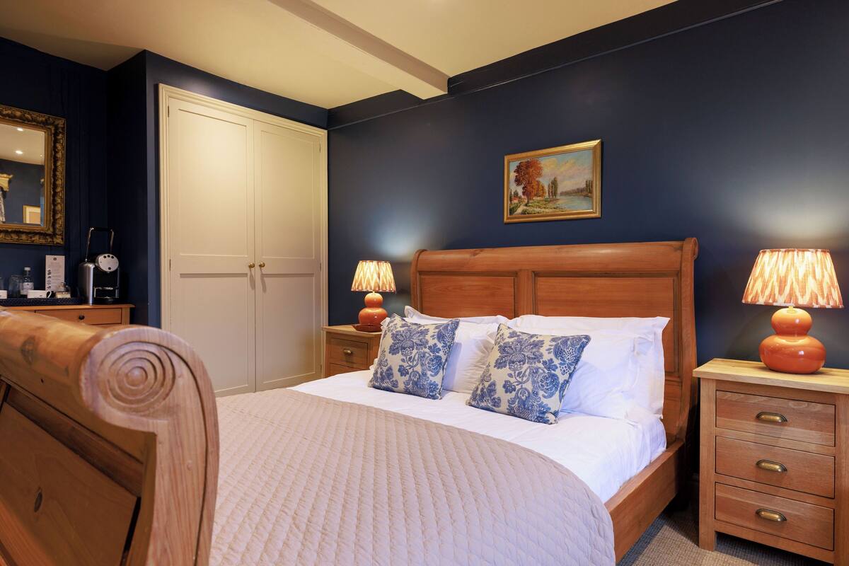 A bedroom with a wooden bed, two bedside tables with lamps, a wardrobe, and a painting on the wall.