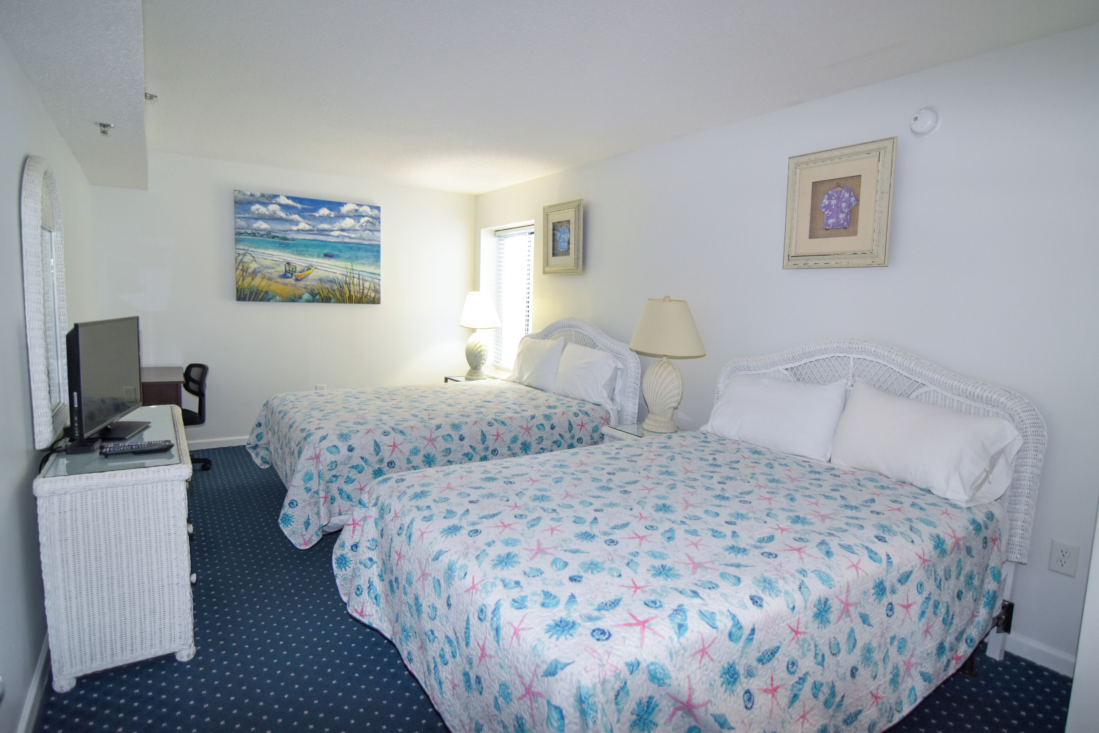 Habitación de hotel con dos camas, un escritorio con computadora, un televisor y un cuadro en la pared.