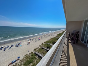A balcony with a view of a beach, beach umbrellas, and a wooden deck. - 20% off week Aug. 15-Aug. 22 Crescent Shores 3BR 3BA OF condo. Amazing views! (North Myrtle Beach)