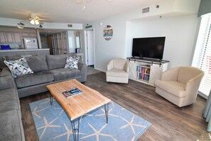 Un salon avec un canapé gris, une table basse en bois, un fauteuil beige et un meuble TV sur lequel sont posés des livres.