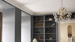 Een woonkamer met een bank, een bijzettafeltje, een sierlijke kroonluchter en een inbouwkast met diverse objecten.