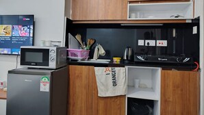Eine kompakte Küche mit Mikrowelle, Toaster und Gasherd. Über der Arbeitsfläche befindet sich ein Holzschrank und eine kleine Ablage mit Küchenutensilien.