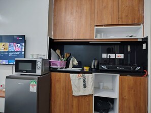 Eine kompakte Küche mit Mikrowelle, Toaster und Gasherd. Über der Arbeitsfläche befindet sich ein Holzschrank und eine kleine Ablage mit Küchenutensilien.