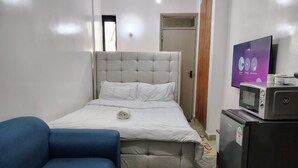 Ein Schlafzimmer mit einem Bett, einem blauen Sessel, einem kleinen runden Tisch, einer Mikrowelle und einem Kühlschrank.