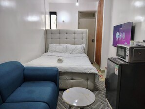 Ein Schlafzimmer mit einem Bett, einem blauen Sessel, einem kleinen runden Tisch, einer Mikrowelle und einem Kühlschrank.