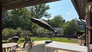 Eine Terrasse im Freien mit Grill, Stühlen, Tisch und einem großen Sonnenschirm.