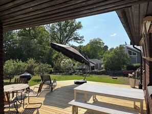 Eine Terrasse im Freien mit Grill, Stühlen, Tisch und einem großen Sonnenschirm.
