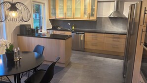 Eine moderne Küche mit Holzschränken, einem Edelstahlkühlschrank und einem Essbereich mit rundem Tisch und Stühlen.