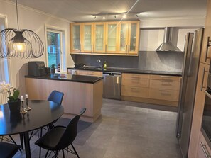 Eine moderne Küche mit Holzschränken, einem Edelstahlkühlschrank und einem Essbereich mit rundem Tisch und Stühlen.