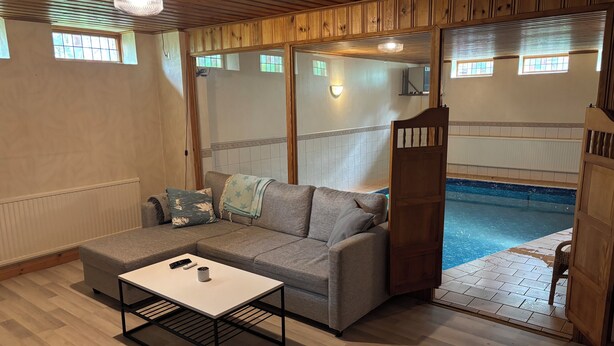Ein Zimmer mit grauem Sofa, einem kleinen Tisch, einer Holztür und Blick auf einen Swimmingpool.