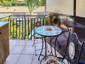 A balcony with a tiled floor, a round table with a patterned tablecloth, and a chair with a decorative backrest. - Loving Gift - Giardini Naxos (Giardini Naxos)